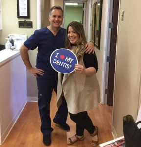 Dr. August de Oliveira with a female patient holding I love my dentist sign beside a man