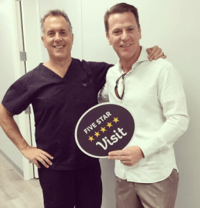 Dr. August de Oliveira with a male patient holding five star visit sign beside a man