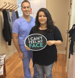Dr. August de Oliveira with a female patient holding I can't feel my face sign
