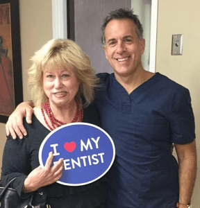 Dr. August de Oliveira with a female patient holding I love my dentist smiling
